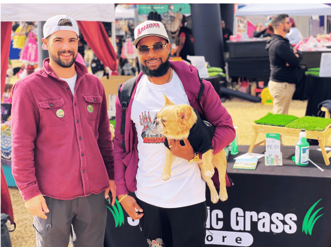 Two men and a dog standing in front of The Synthetic Grass Store booth at the Doggie Street Festival in Phoenix.